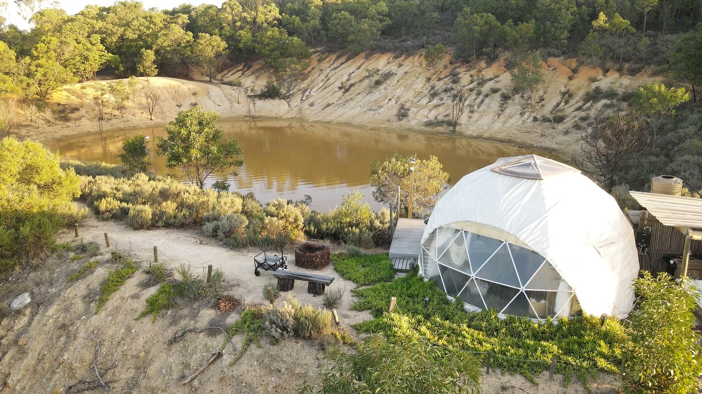 Geodesic dome accommodation overlooking a natural water lagoon surrounded by rugged hillsides and vegetation