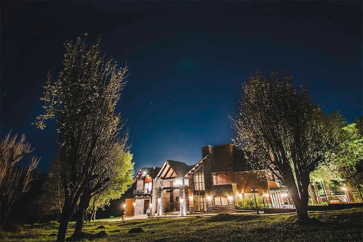 Tudor-style cabin lit at night with tall trees and starry sky