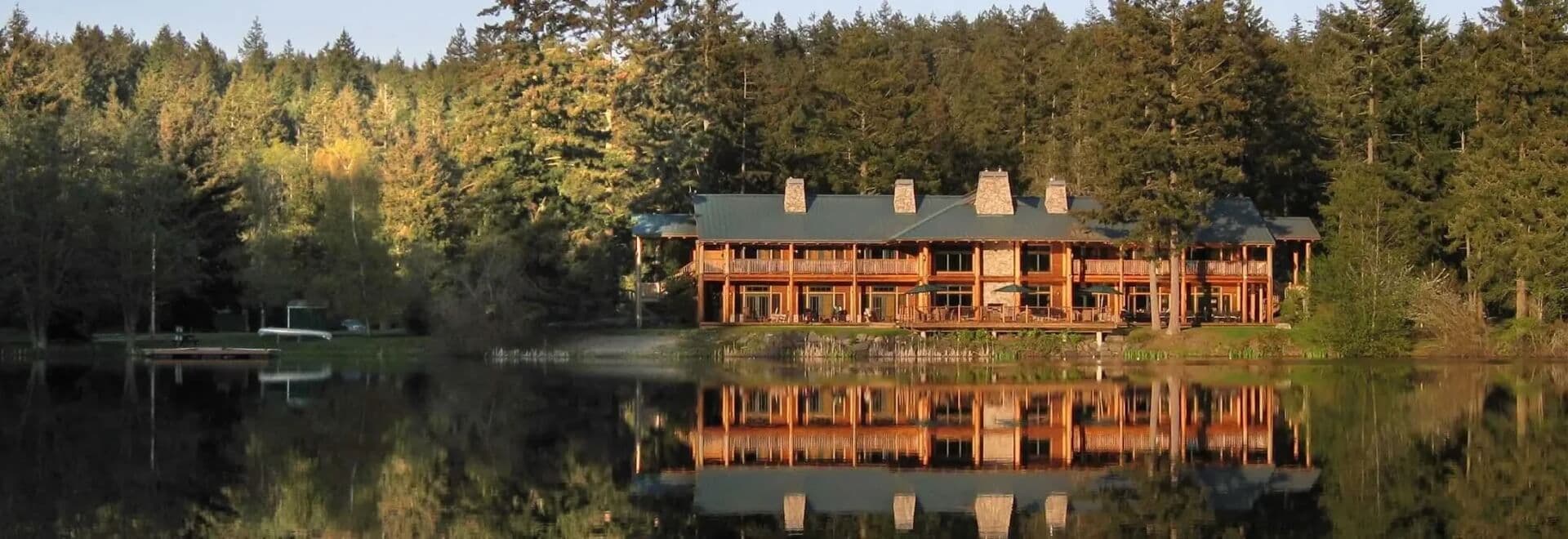 Lakeside lodge with red-brick chimney reflected in calm water, surrounded by forest