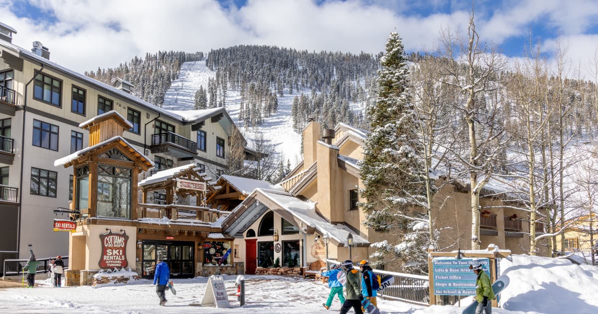 Snowy mountain resort base with lodge buildings and ski slopes in background