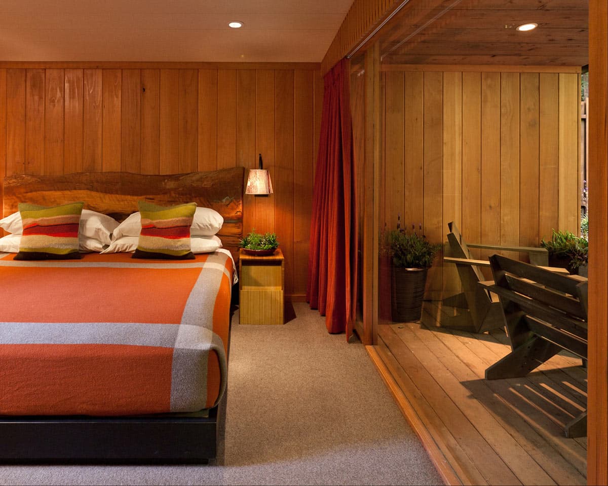 Spa bedroom with wood-paneled walls, orange bedding, and direct access to outdoor seating area