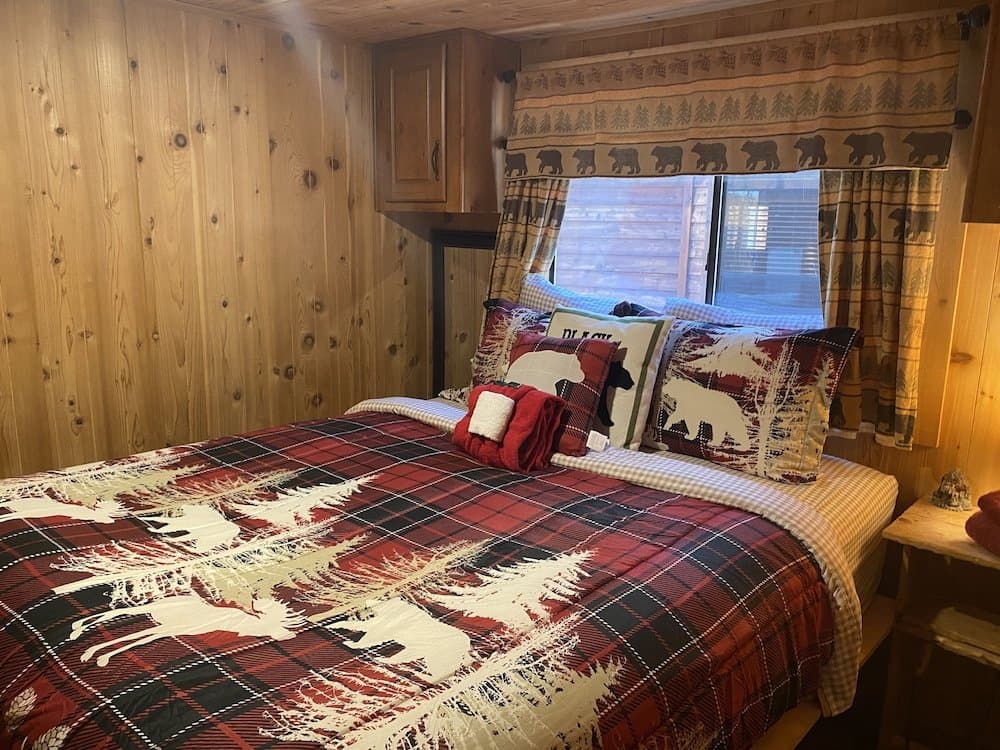 Cozy cabin bedroom with knotty pine walls, bear-themed bedding, and lake view through large windows