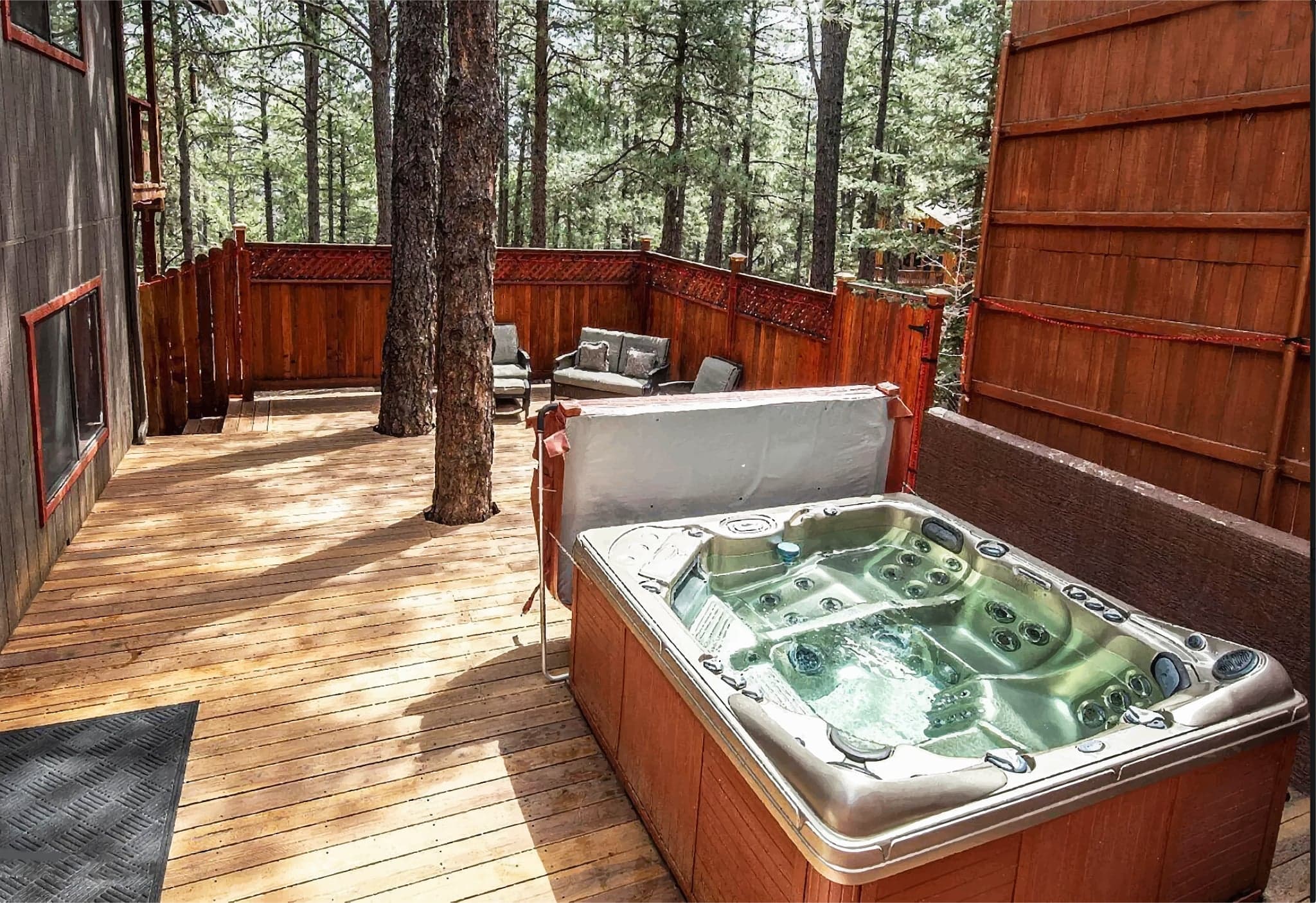 Hot tub on wooden deck surrounded by tall pine trees in forest setting