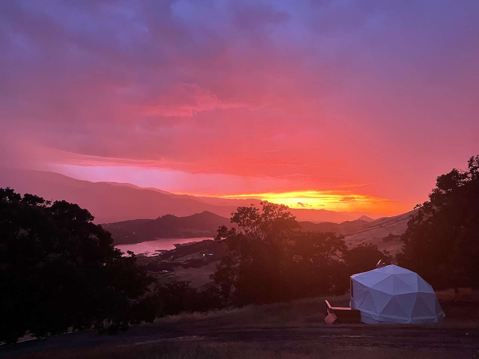 Glamping dome at sunset with mountains and water view at dusk