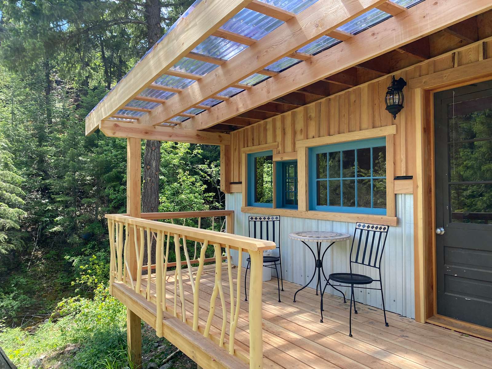Modern wooden cabin with blue-trimmed windows and polycarbonate pergola on forest deck