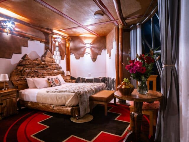 Luxurious bedroom with carved wooden bed frame, red geometric rug, and mountain landscape wall mural