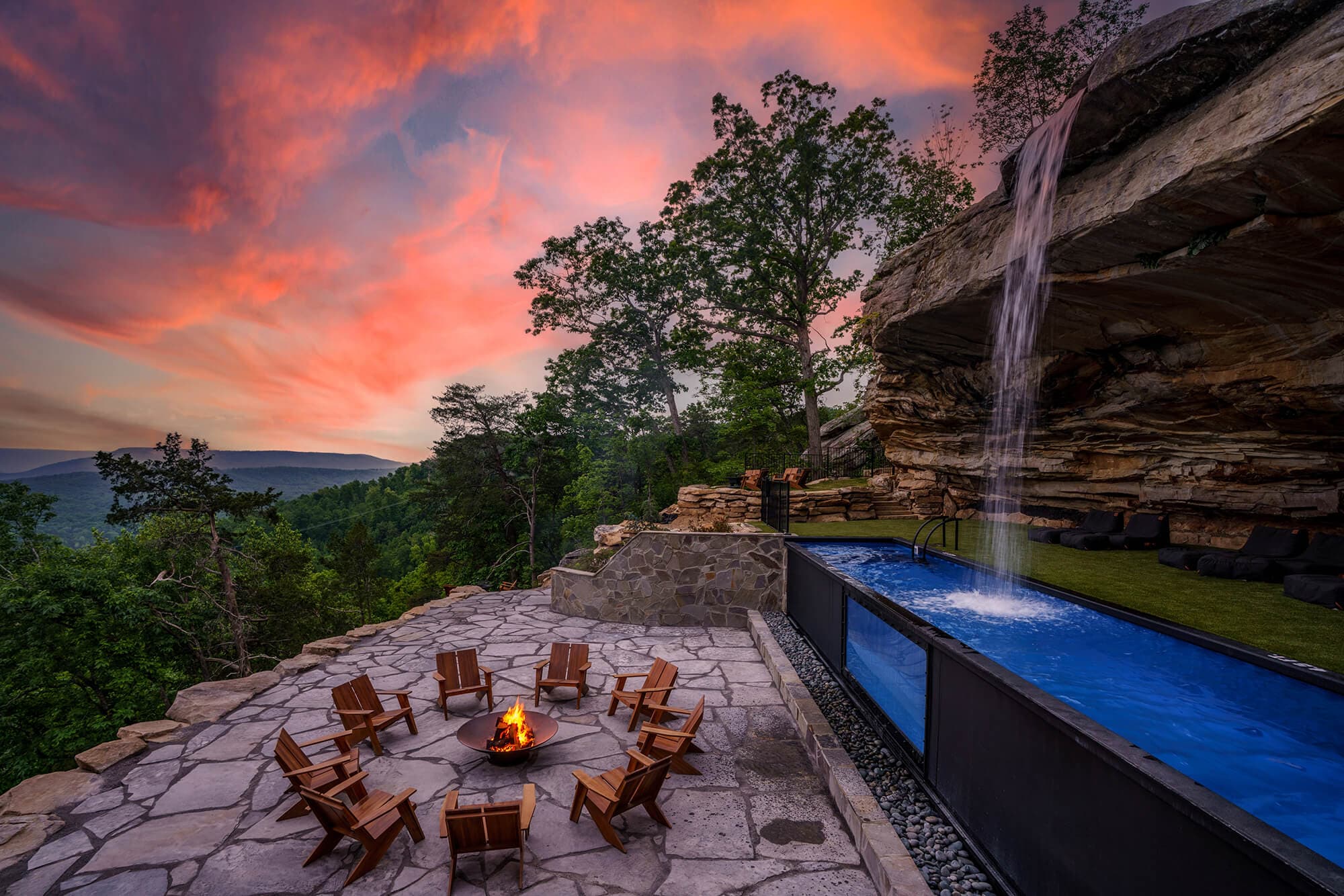 Outdoor infinity pool waterfall at sunset with fire pit, Adirondack chairs, and mountain views