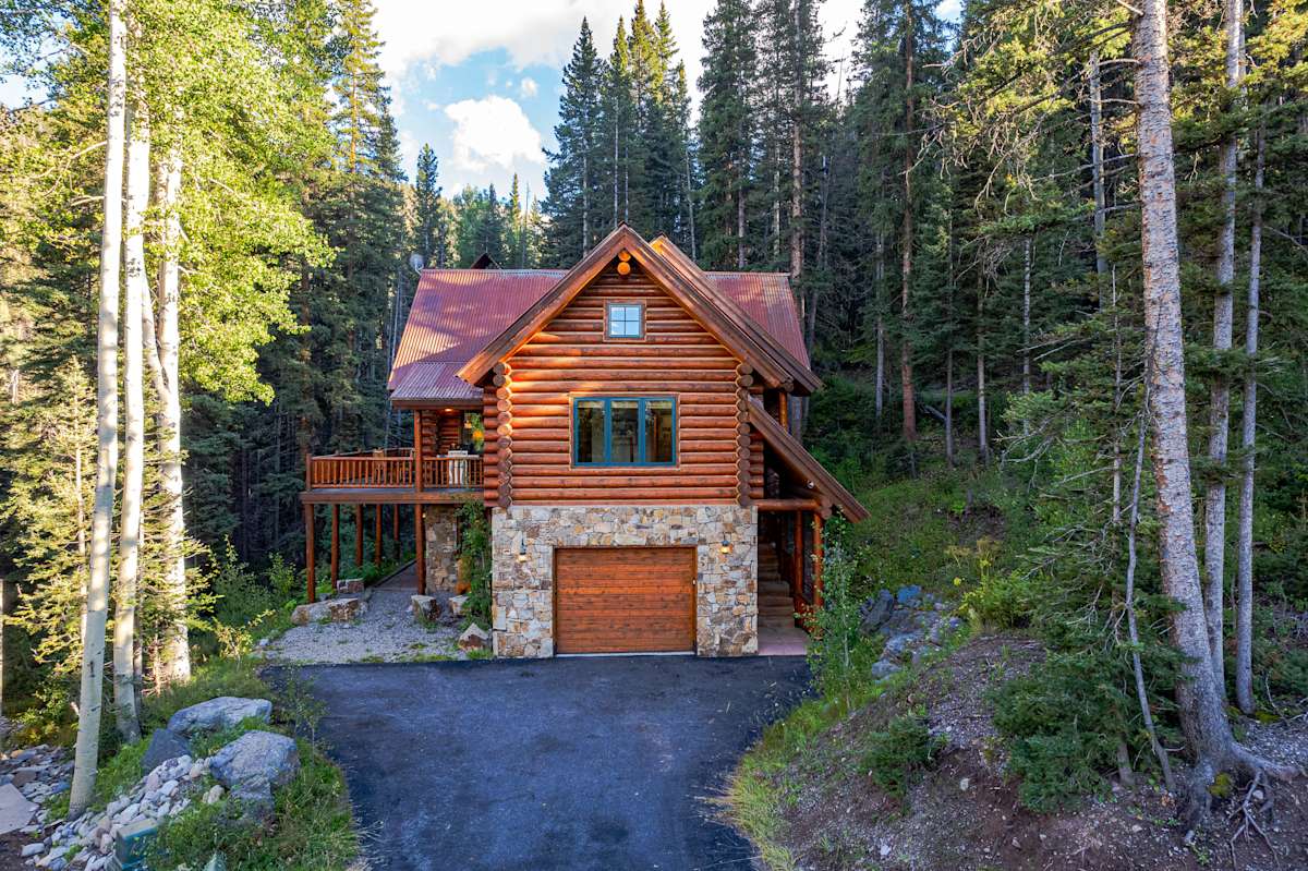 Modern log cabin with red metal roof nestled in dense forest surrounded by tall pine trees