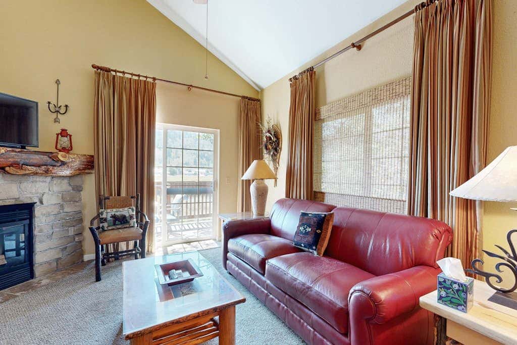 Spacious living room with red leather sofa, fireplace, and doors opening to balcony