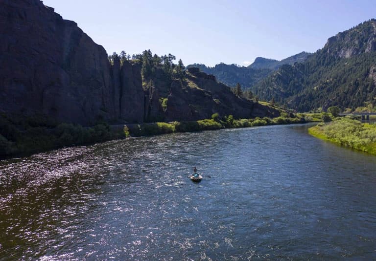 River with rocky canyon walls and forested mountains in bright sunlight