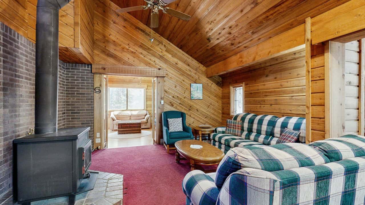 Spacious log cabin interior with wood ceilings, fireplace, and plaid furnishings