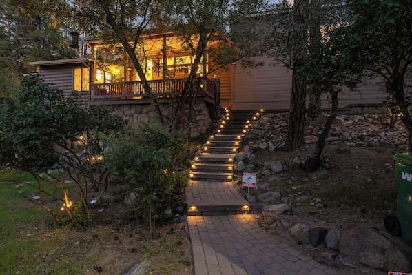 Illuminated treehouse structure with glowing windows and lit pathway through trees at dusk