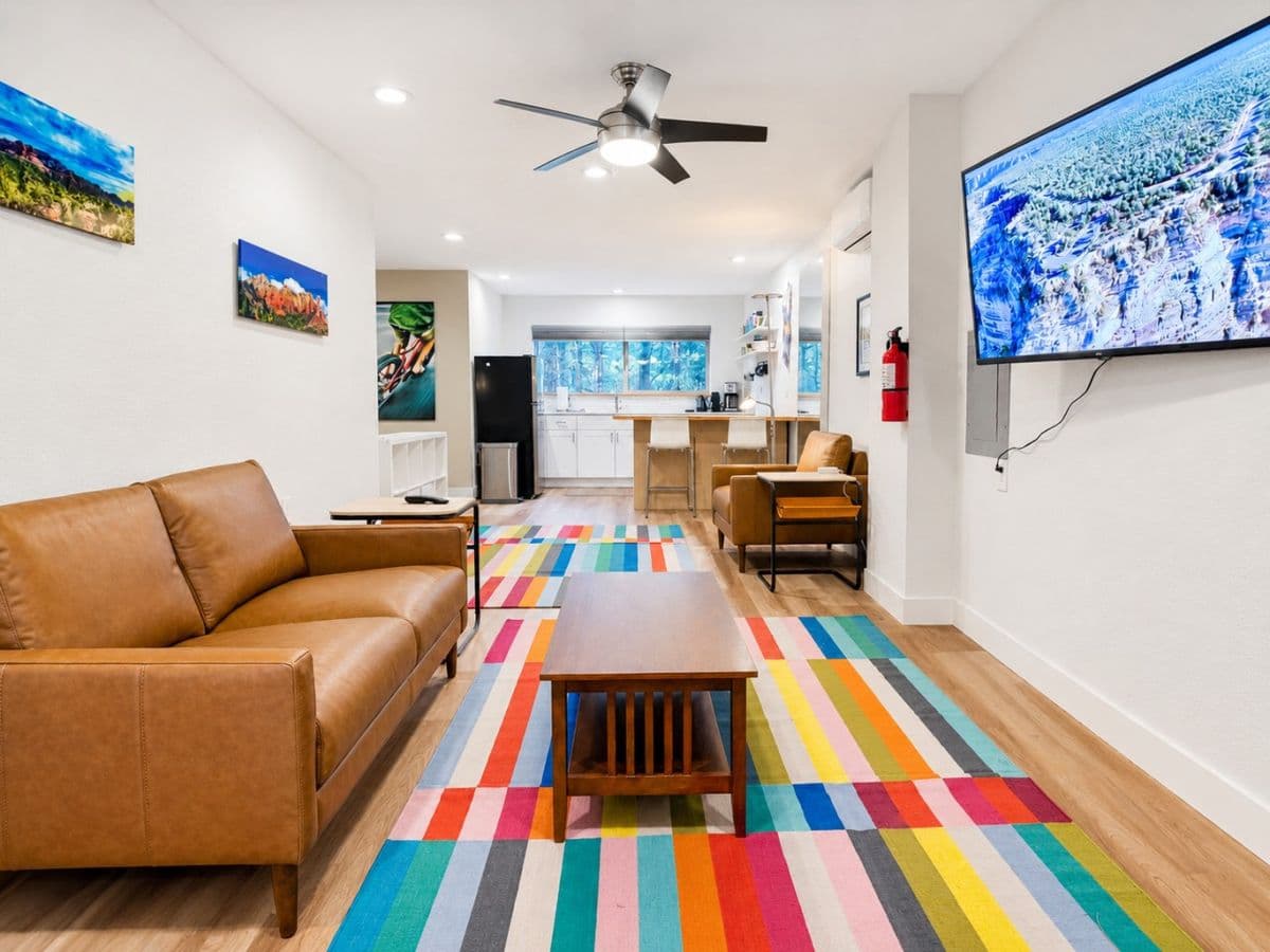 Bright common room with leather sofa, colorful striped rug, kitchenette, and landscape artwork