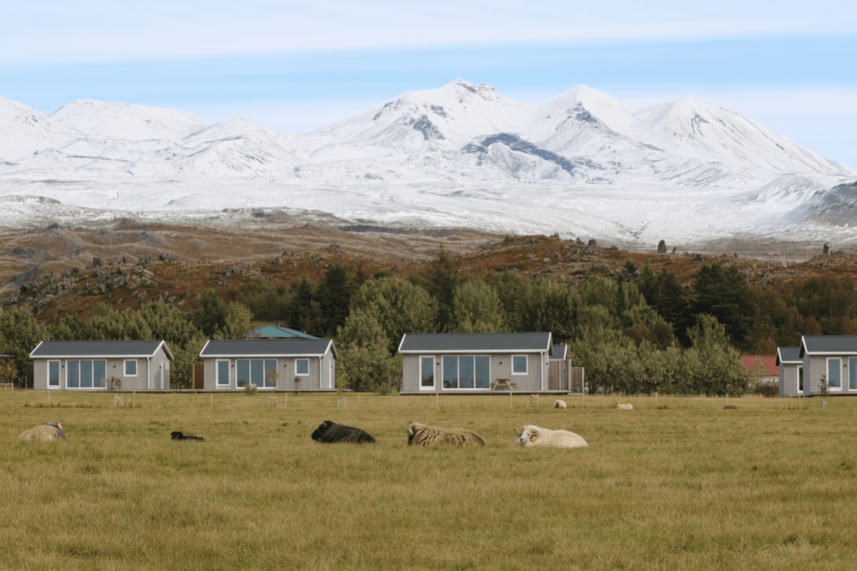 Modern cabins with snow-capped volcanic peaks and tundra landscape in background