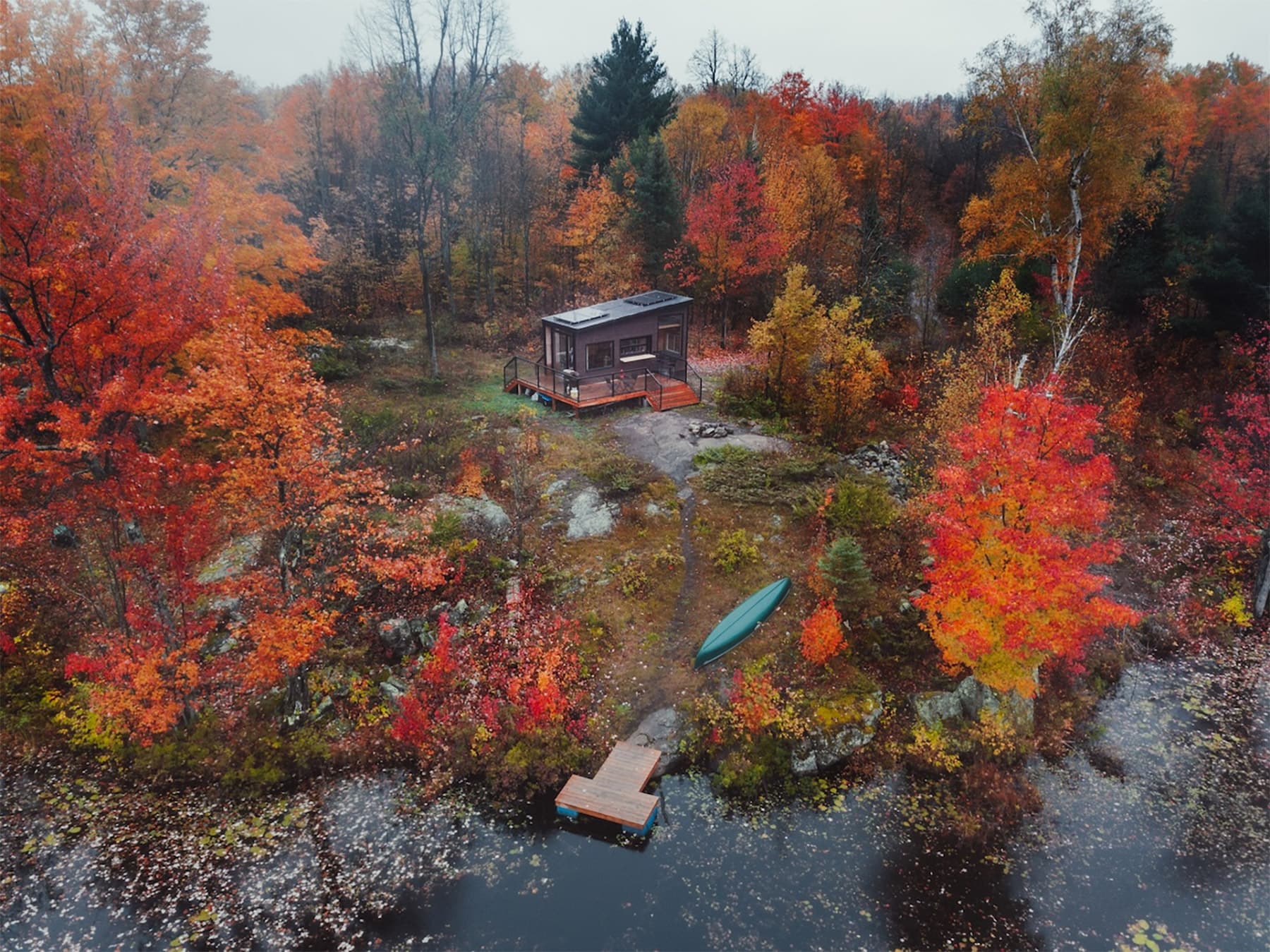 Wooden cabin surrounded by vibrant red and orange autumn foliage beside a serene pond with kayaks