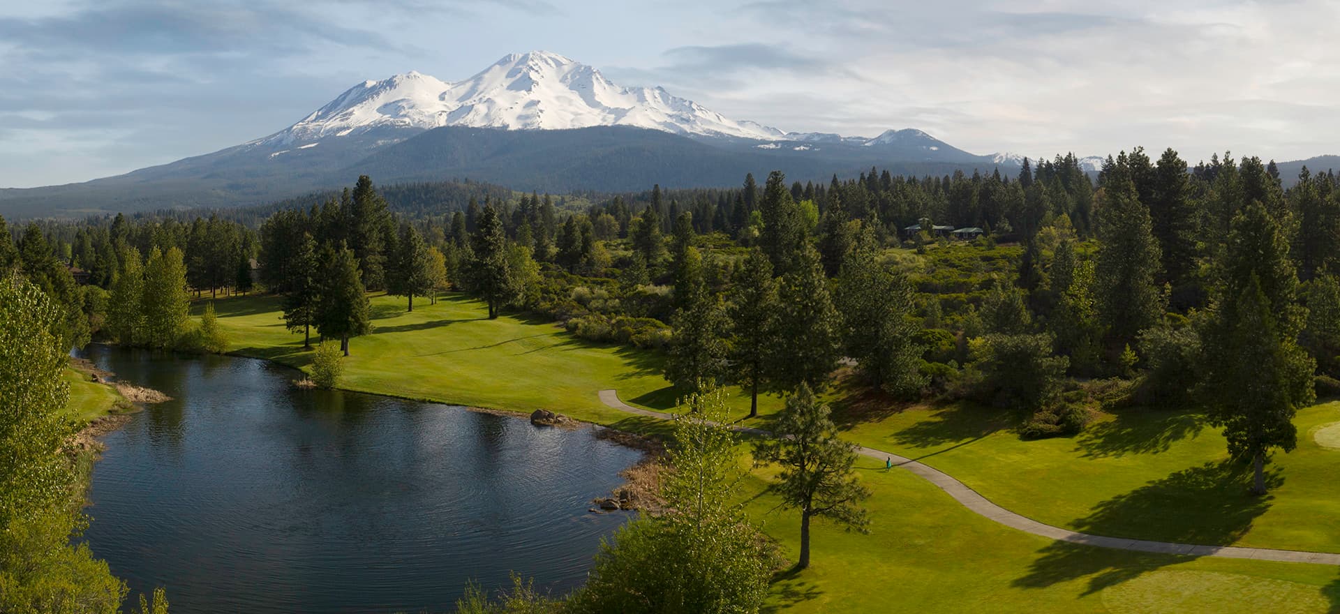 Snow-capped Mount Shasta rising above forested grounds with river and manicured lawn