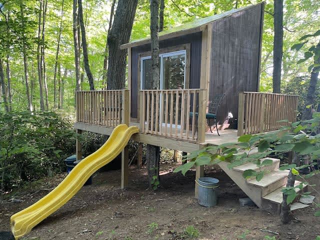 Modern treehouse cabin with wrap-around deck and yellow slide among tall trees