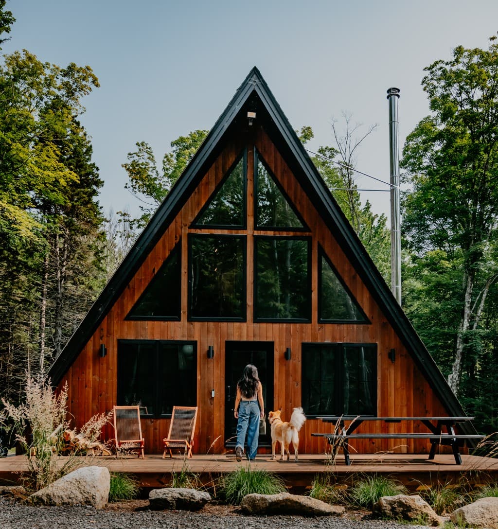 Modern wooden A-frame cabin with large triangular windows in a forested setting