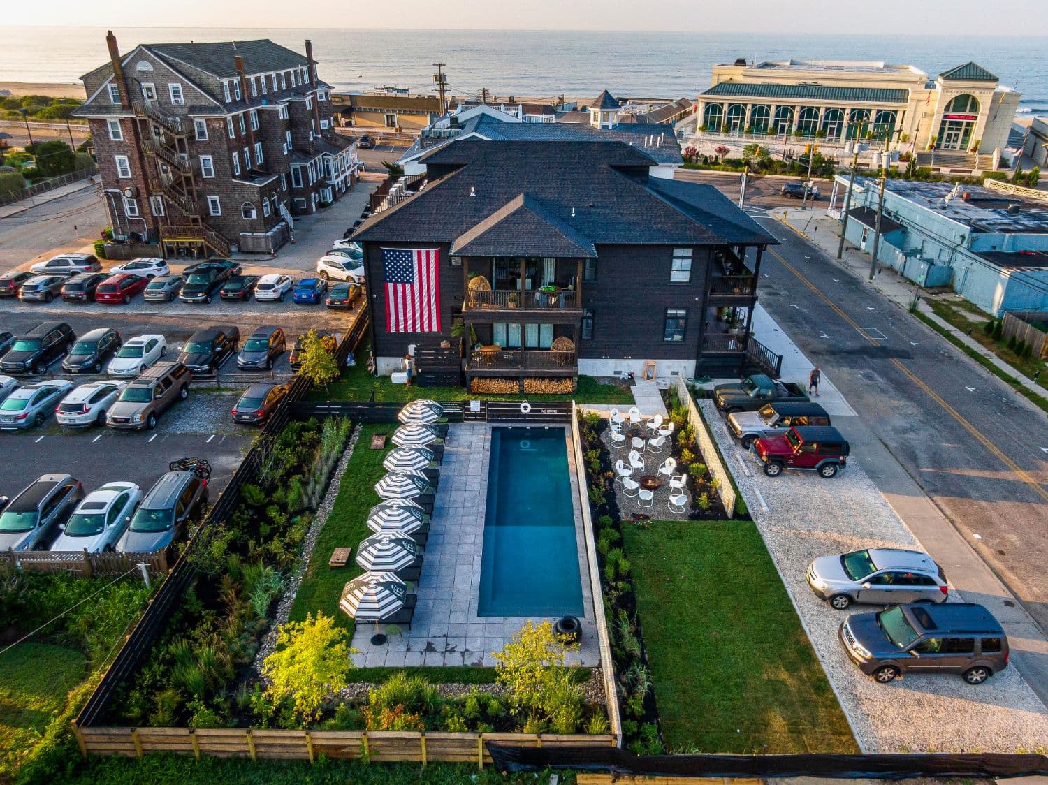 Aerial view of modern spa building with pool, striped umbrellas, and oceanfront setting