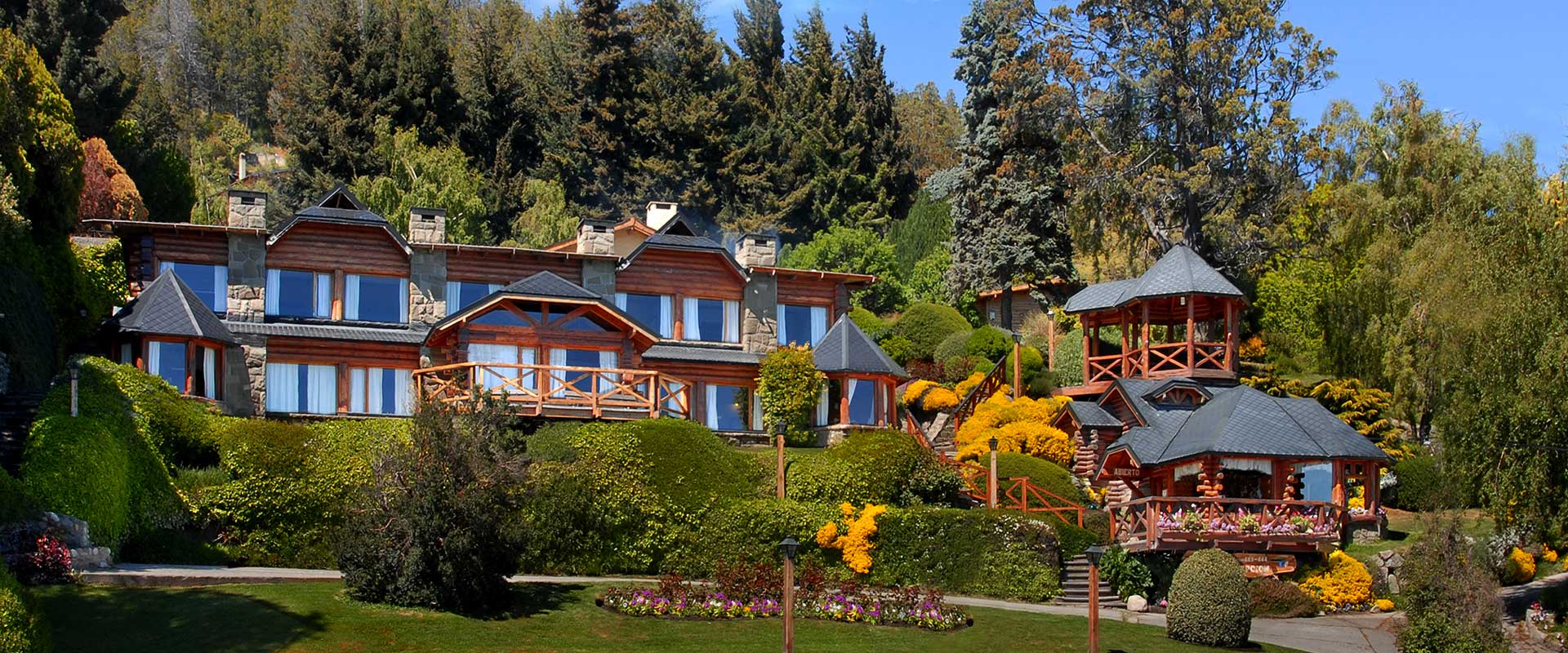 Modern rustic lodge with stone and wood architecture, lush grounds, and gazebo nestled in forested setting