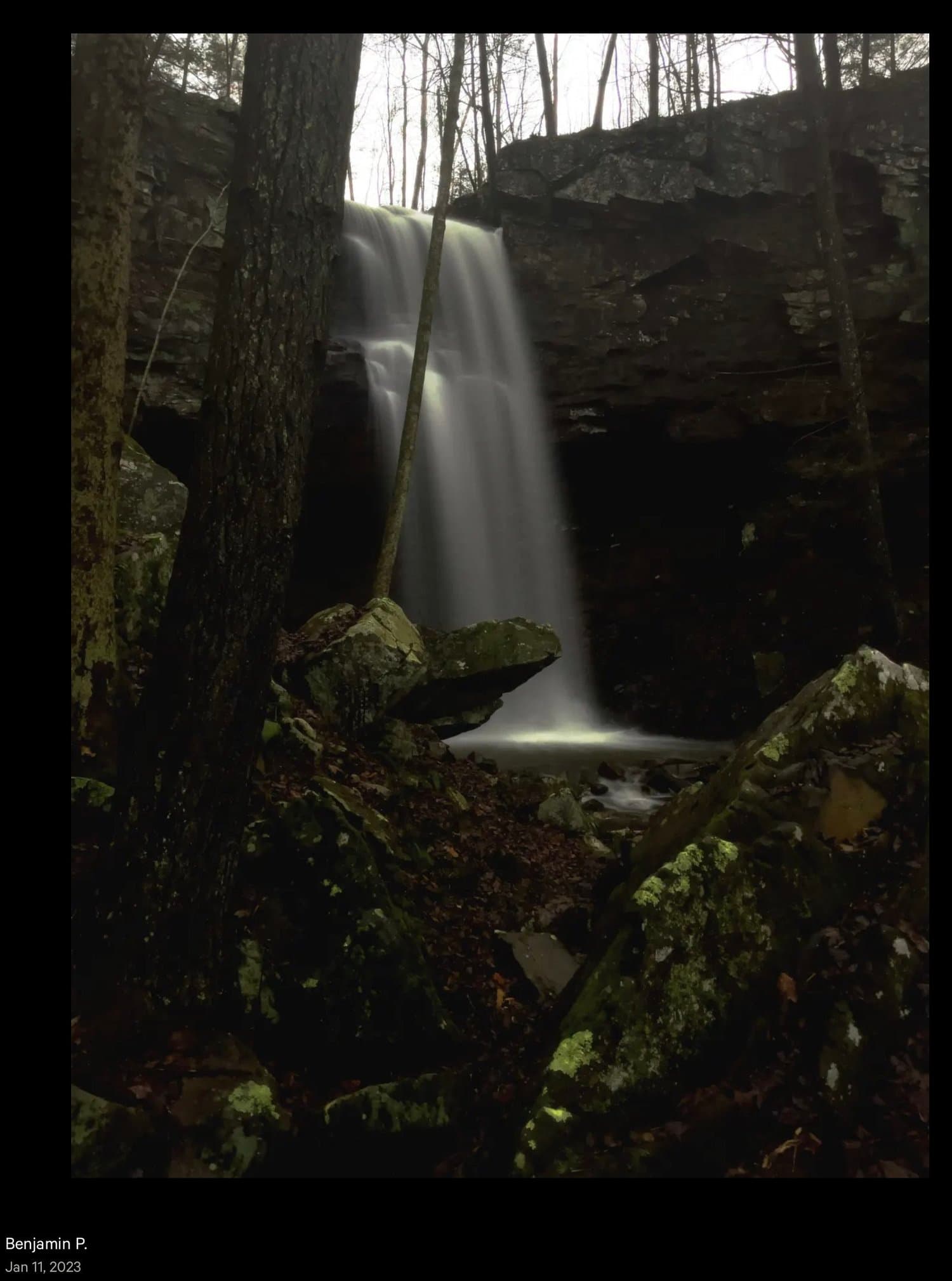 Waterfall cascading into a pool surrounded by moss-covered rocks and bare trees