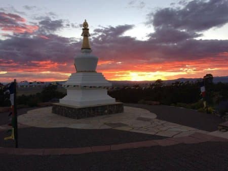 White stupa with golden spire silhouetted against dramatic sunset sky