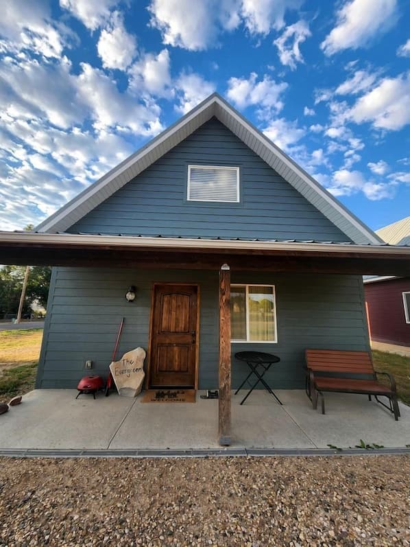 Modern blue cabin with peaked roof and covered porch, situated on gravel under blue sky