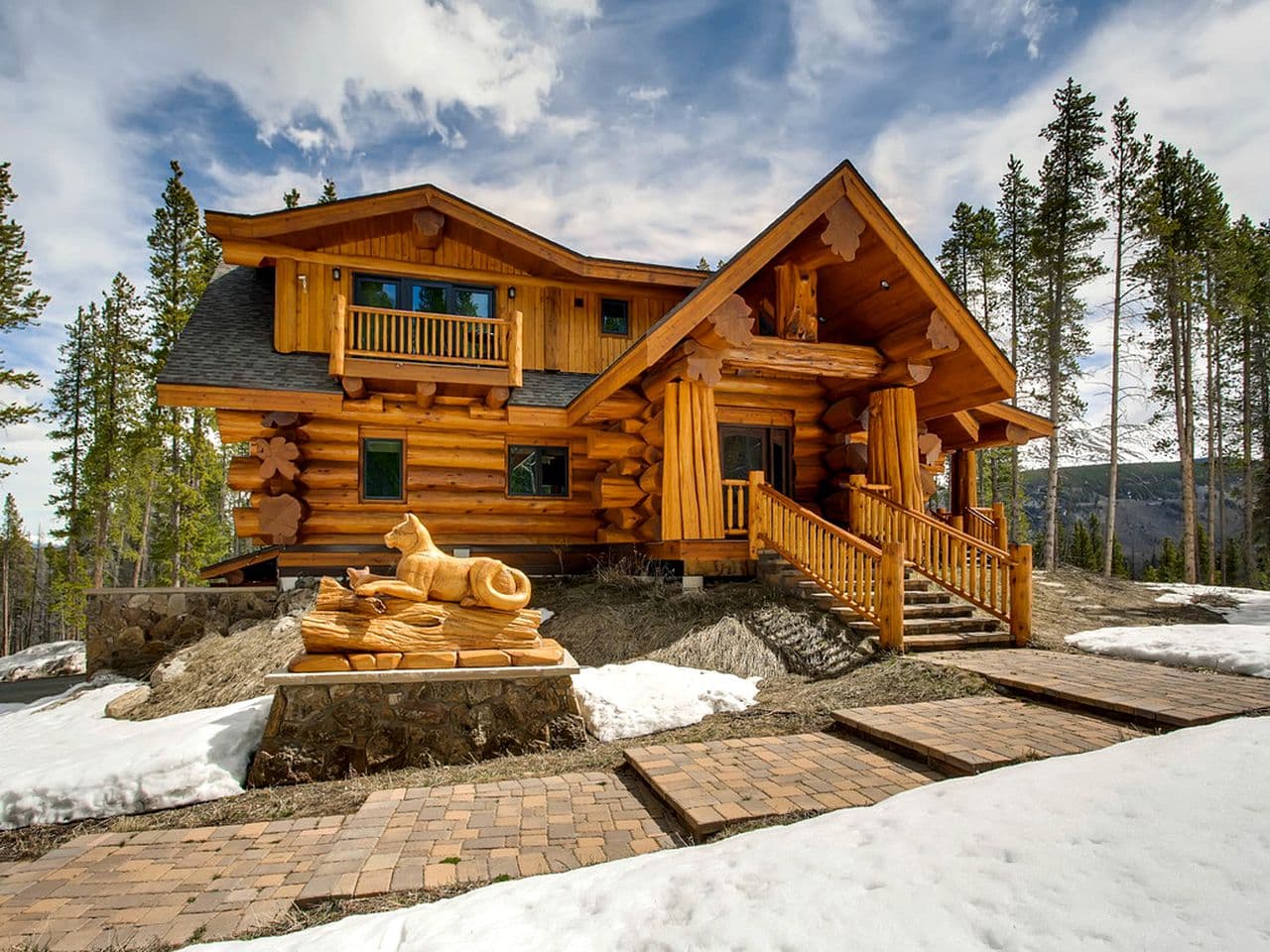 Luxury log cabin exterior with wooden architecture, covered porch, and mountain forest setting