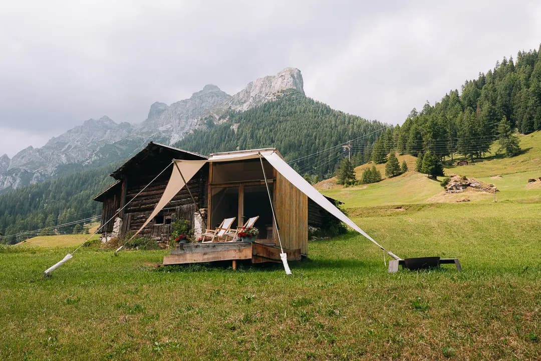 Wooden glamping tent with canvas awning in alpine meadow below mountain peaks
