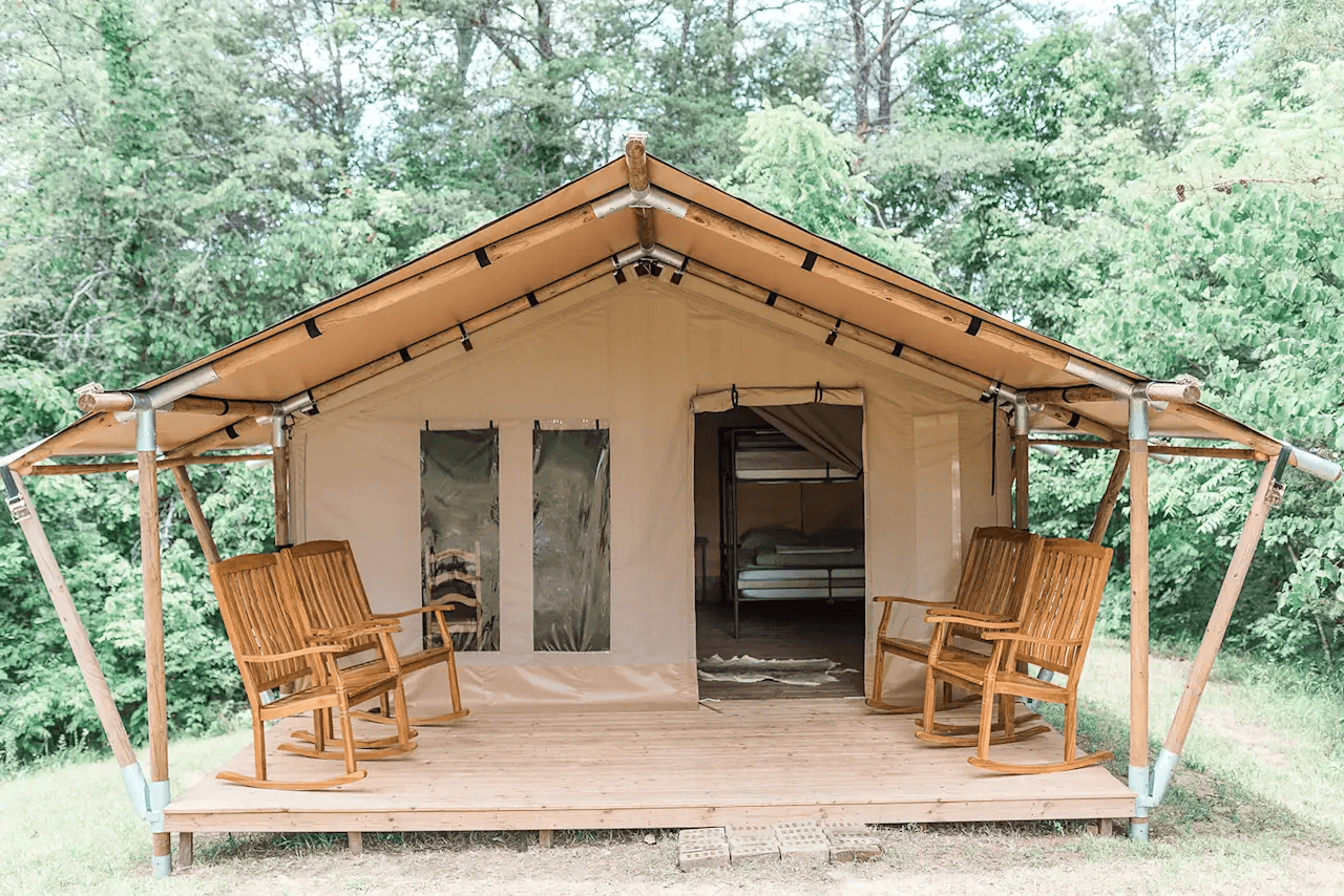 Canvas glamping tent with wooden porch, rocking chairs, and forest backdrop