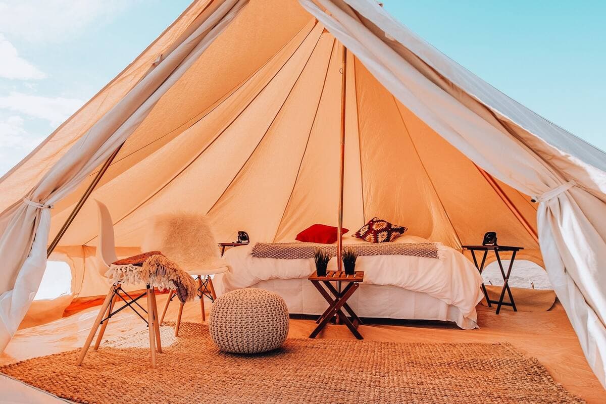 Luxury glamping tent interior with white bed, natural light filtering through orange canvas