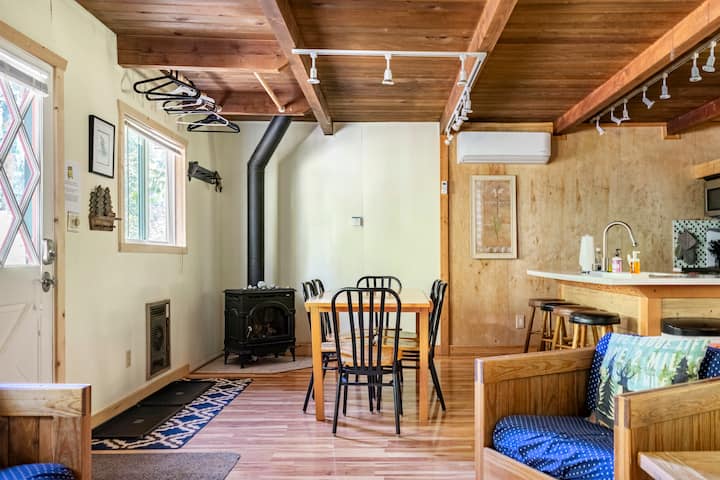 Cabin interior with wood beams, dining table, wood stove, and bunk beds