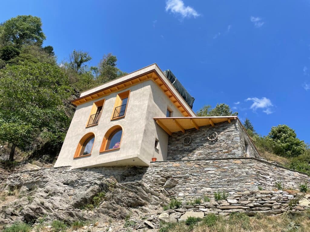 Modern white and stone tiny house on rocky hillside with green landscape and blue sky