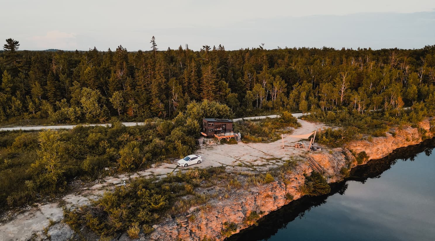Rustic cabin nestled in boreal forest beside a rocky shoreline with red cliffs and calm water