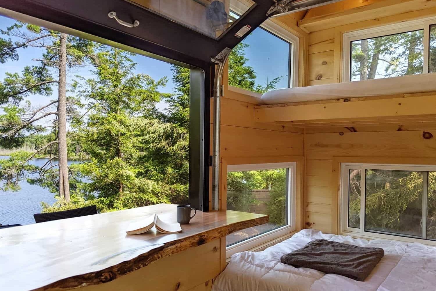 Modern wood cabin bedroom with lake view through floor-to-ceiling windows and natural wood beams
