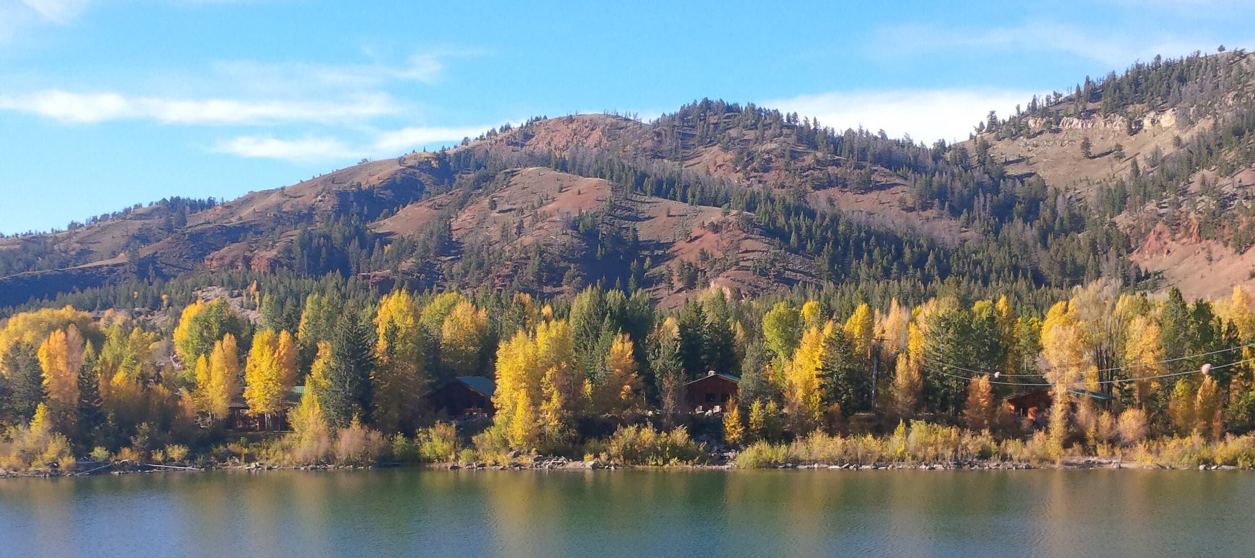 Lake surrounded by forested mountains with autumn aspens, cabins nestled among trees along shoreline