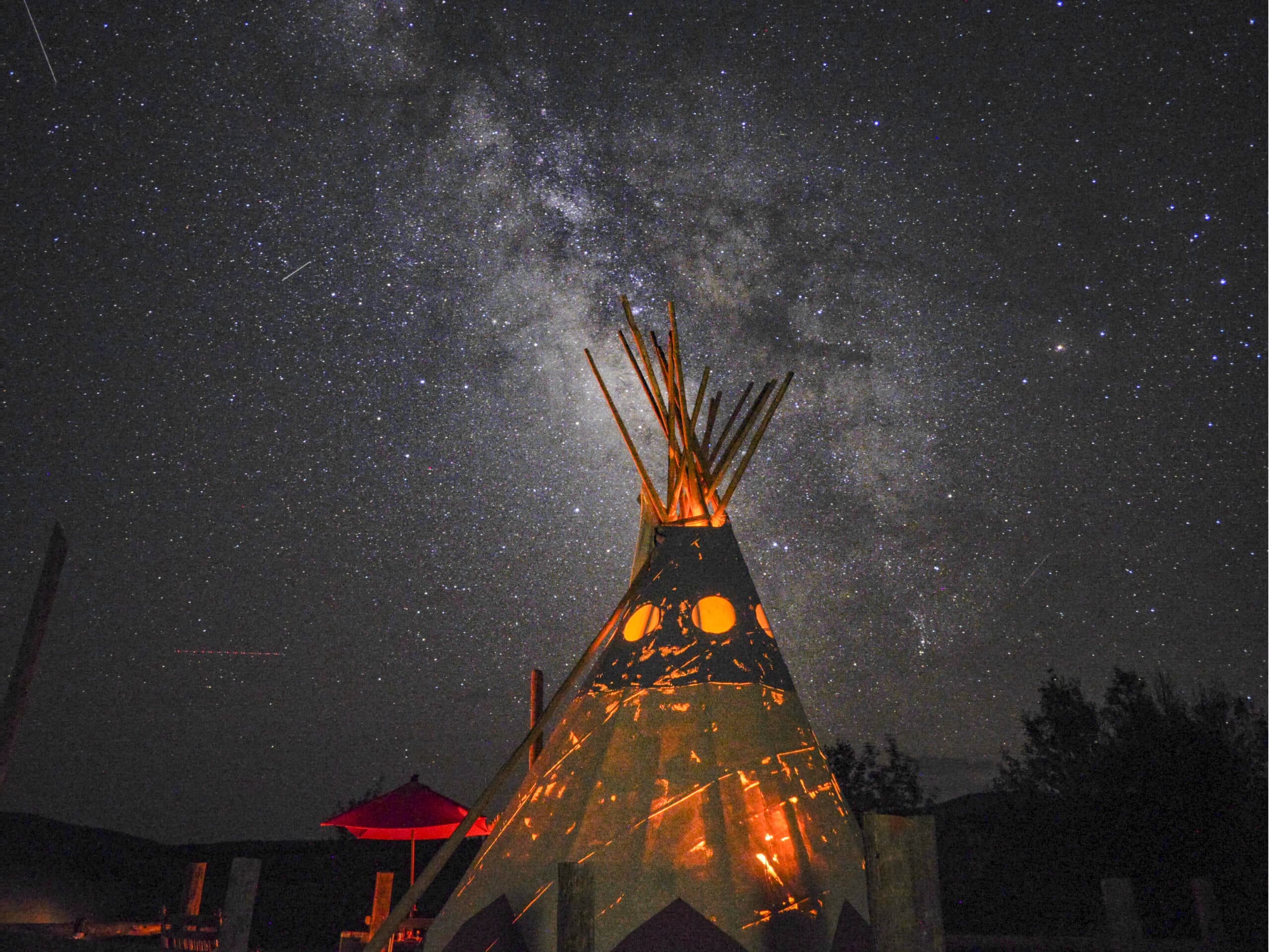 Illuminated tipi against starry night sky with Milky Way visible overhead