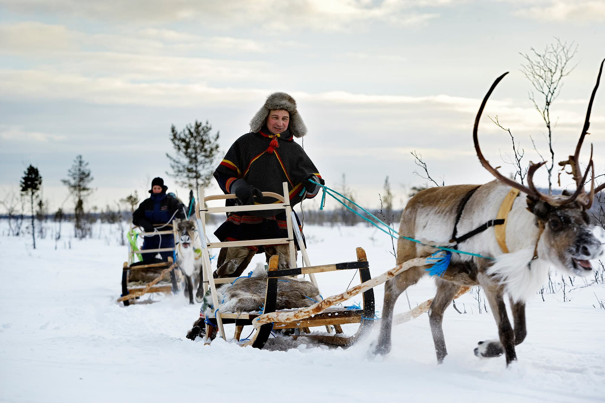 Person on reindeer sledge being pulled by reindeer across snowy landscape