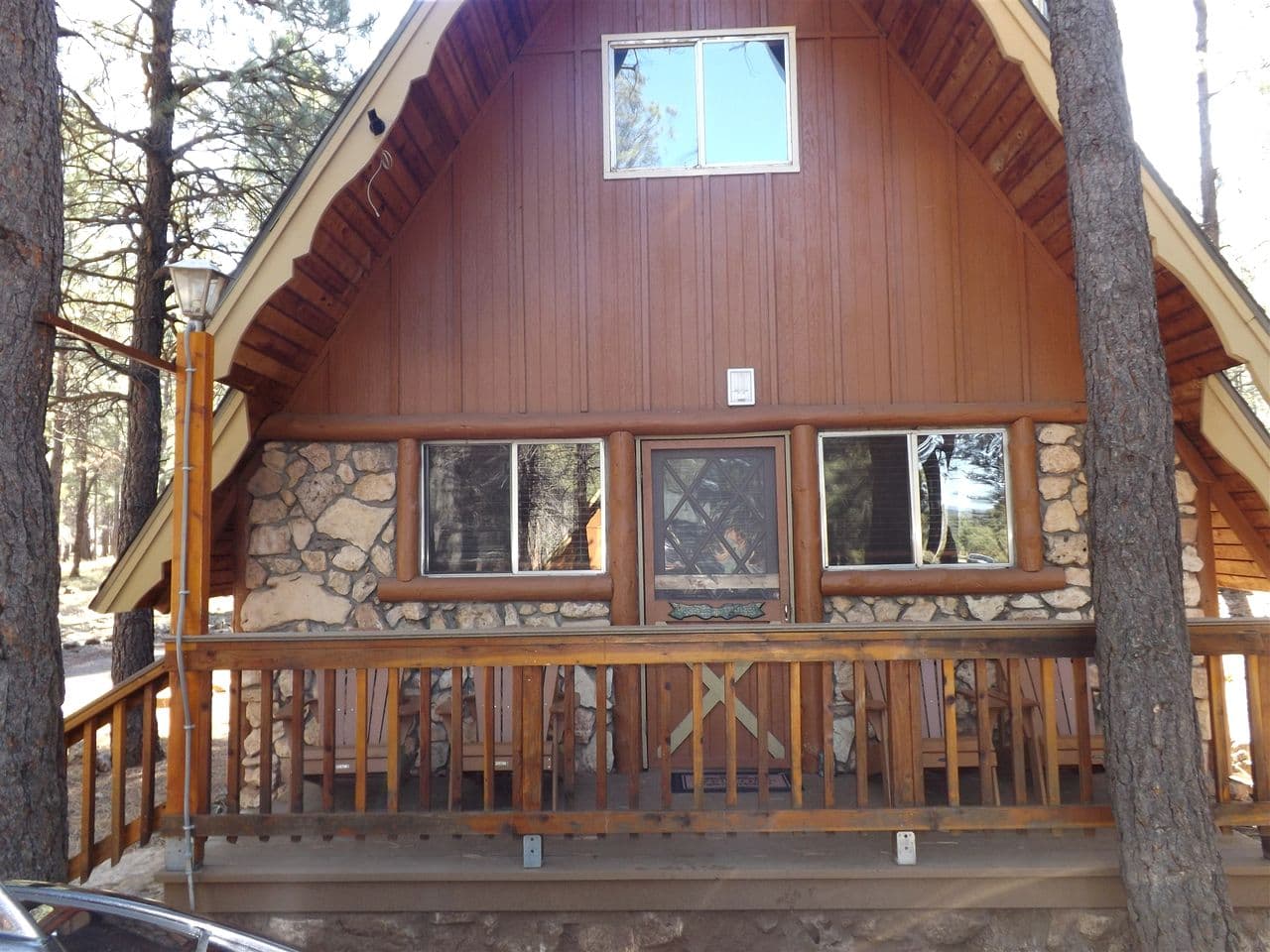 Rustic cabin with stone base, wooden siding, and deck nestled among pine trees