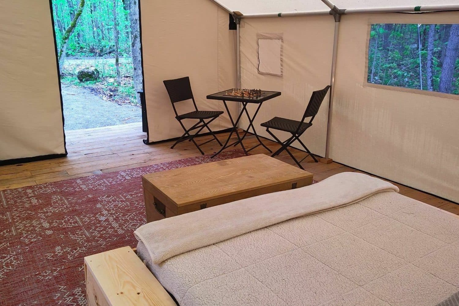 Interior of a glamping tent with massage table, seating area, and forest views through open door