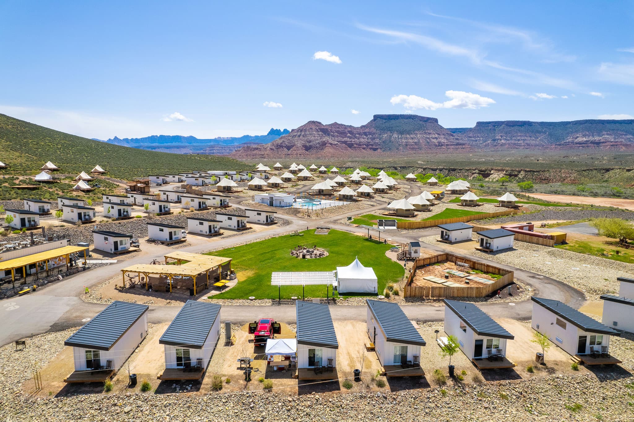 Aerial view of glamping resort with white cabins and safari tents against red rock mountains