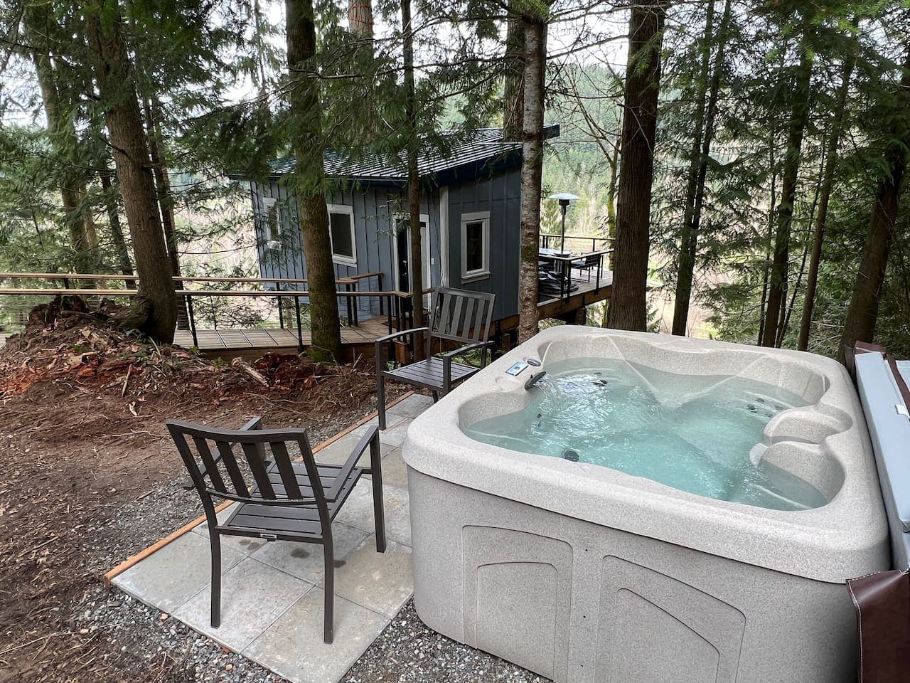 Hot tub with steaming water nestled among tall forest trees with cabin in background