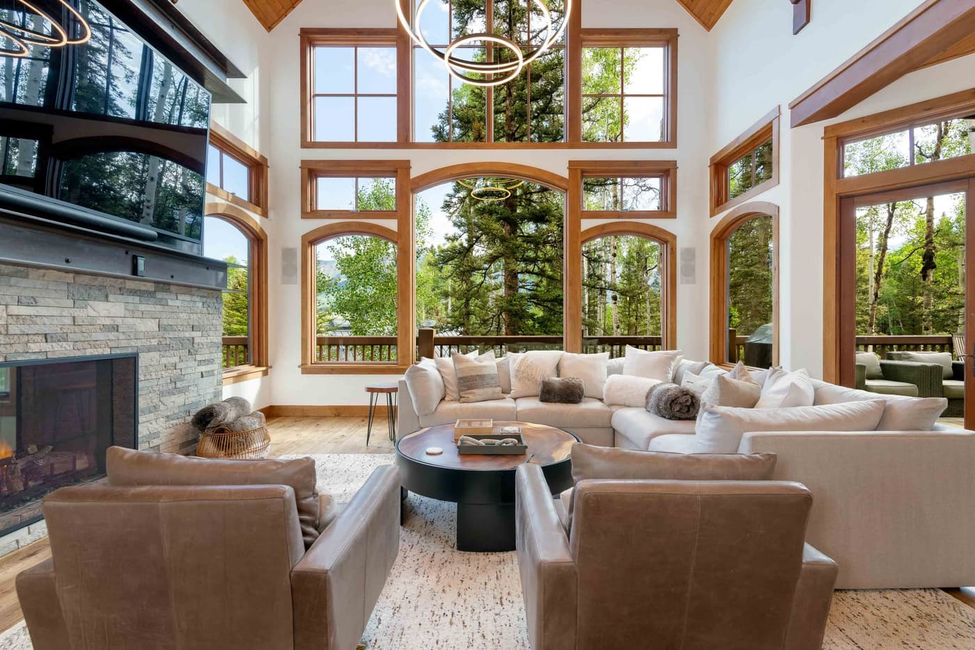 Luxury living room with soaring wood-beamed ceilings, fireplace, and expansive windows overlooking forest