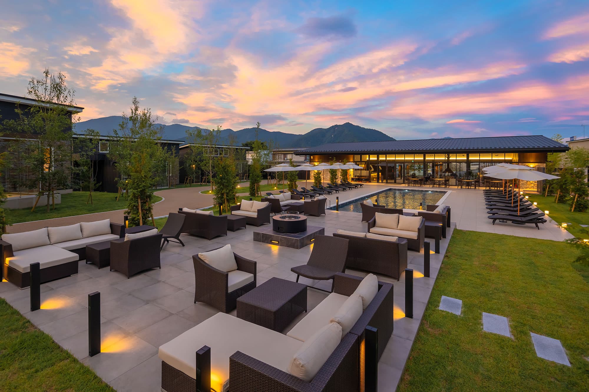 Luxury resort exterior at dusk with outdoor seating, pool, and mountain backdrop