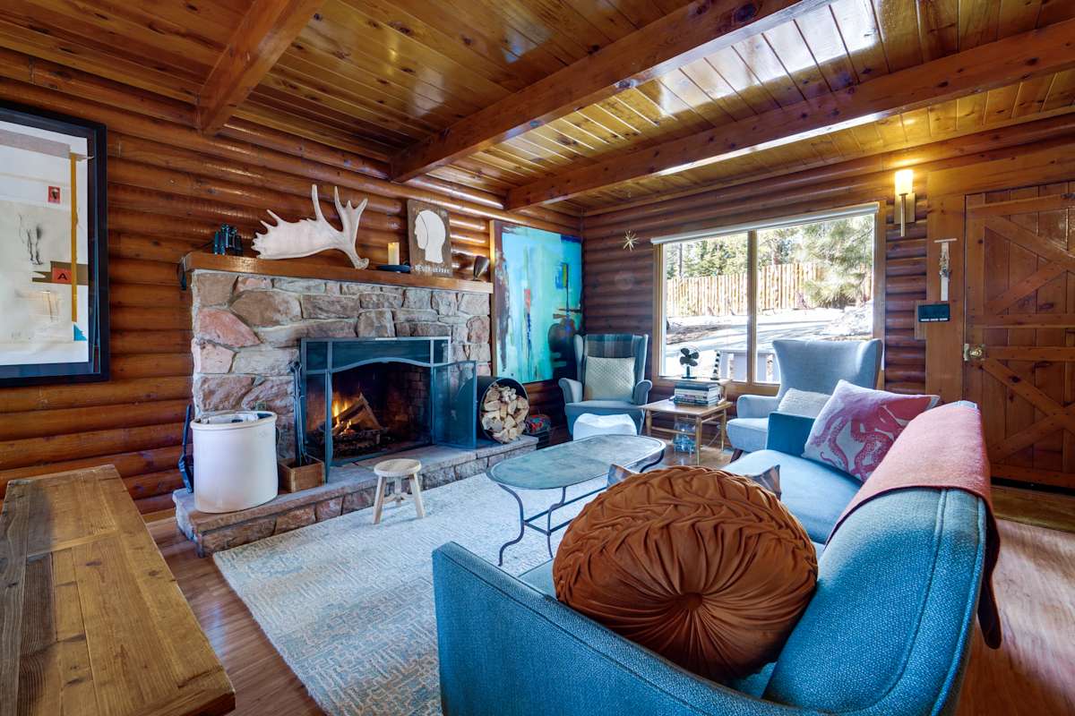Rustic log cabin interior with stone fireplace, blue seating, and wood beam ceiling