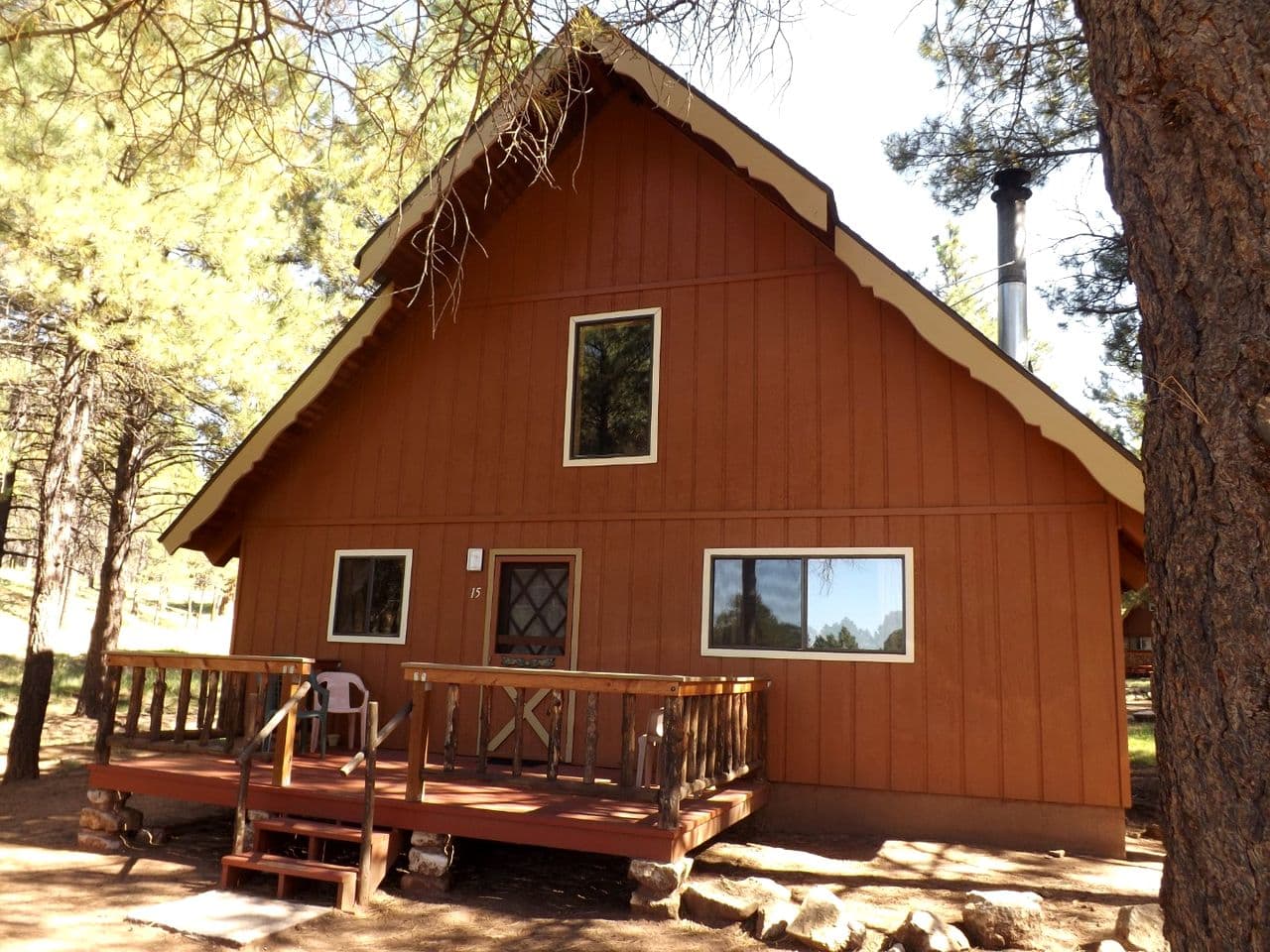 Red-brown cabin with front deck nestled among pine trees in forest setting