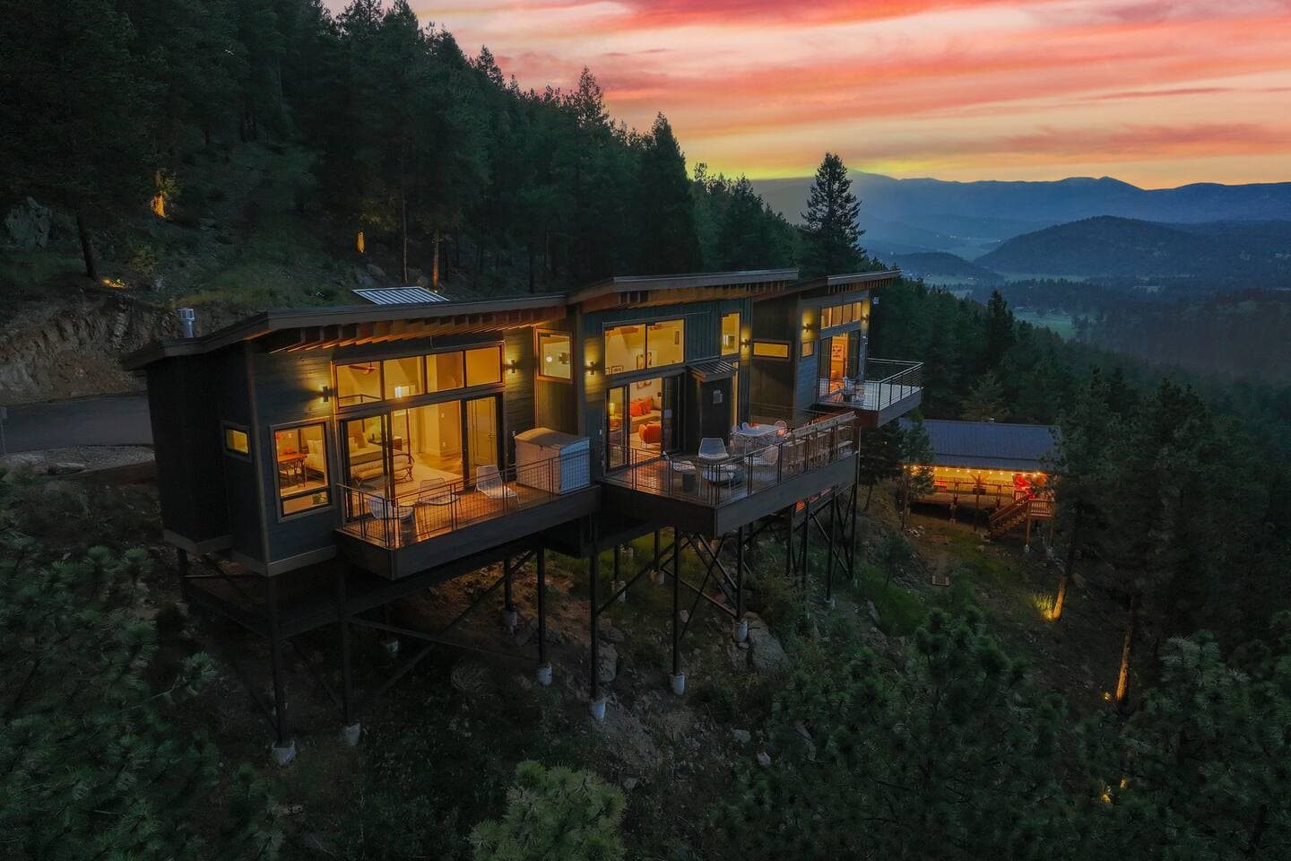Modern treehouse with lit interiors perched on stilts among forests at sunset, mountain vista beyond
