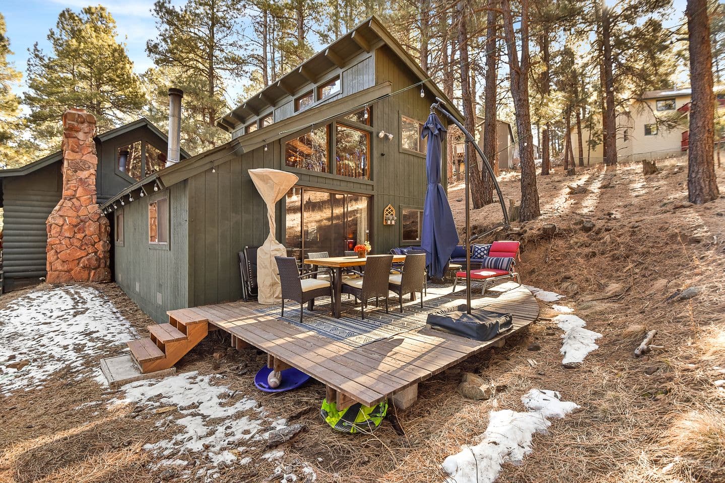 Modern cabin with stone chimney, large windows, and furnished patio among tall pines