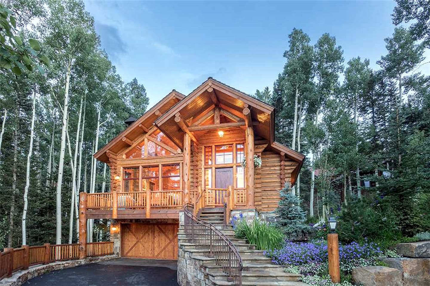 Wooden log cabin with peaked roof and wrap-around deck surrounded by aspen trees