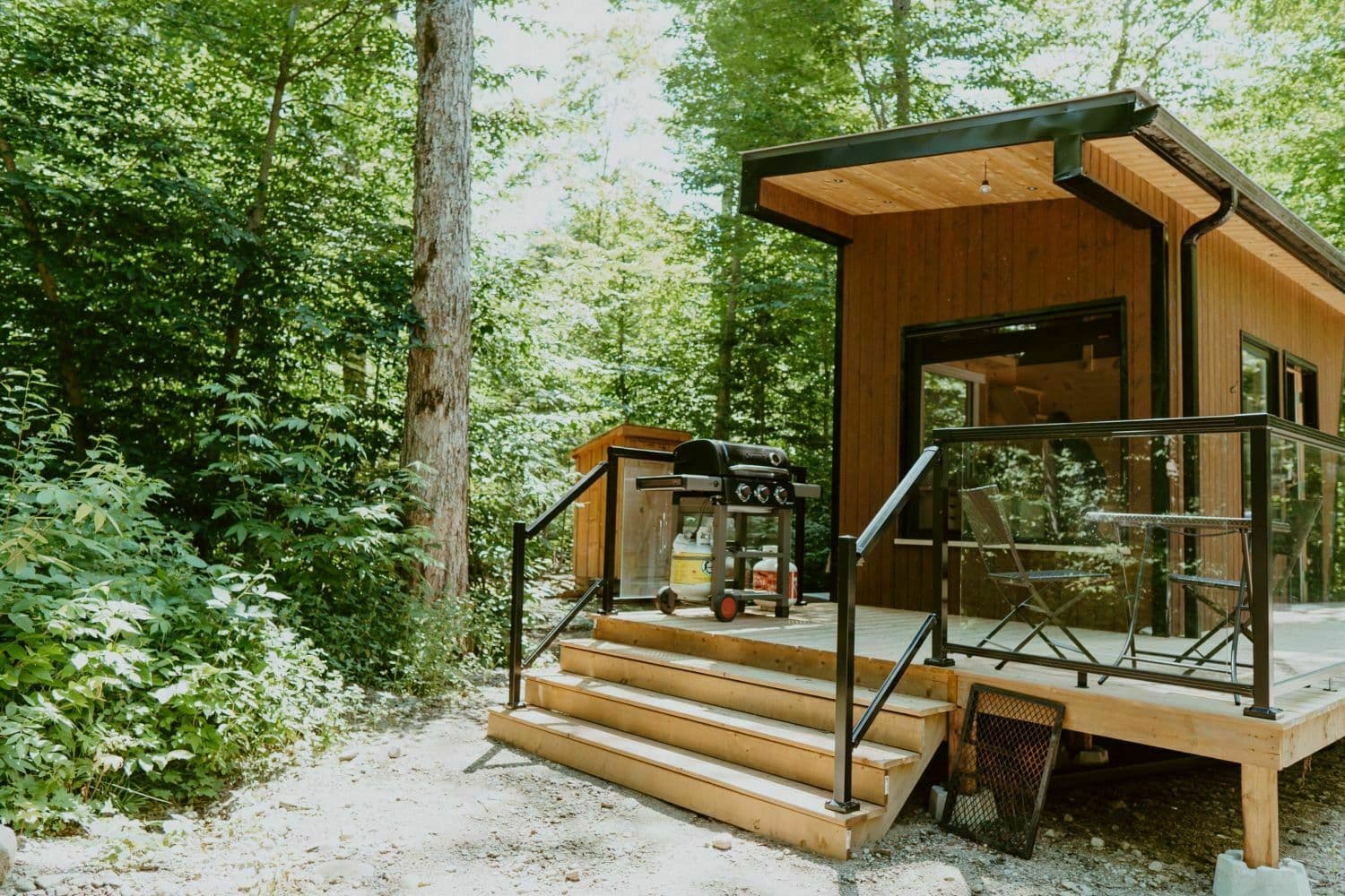Modern wood cabin nestled in forest with deck, grill, and metal railings